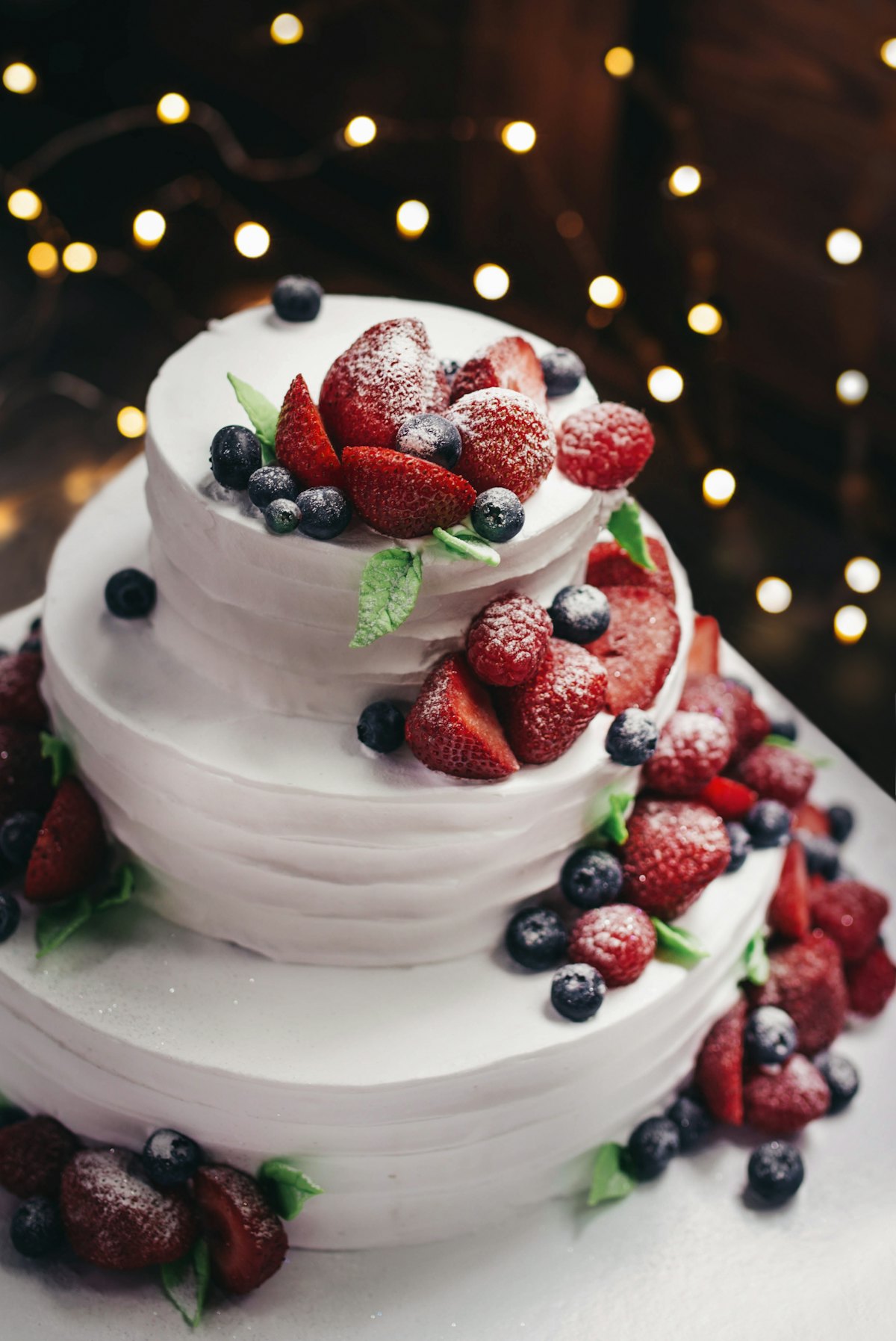 Tort cu două etaje, decorat cu fructe de pădure și lumini în fundal