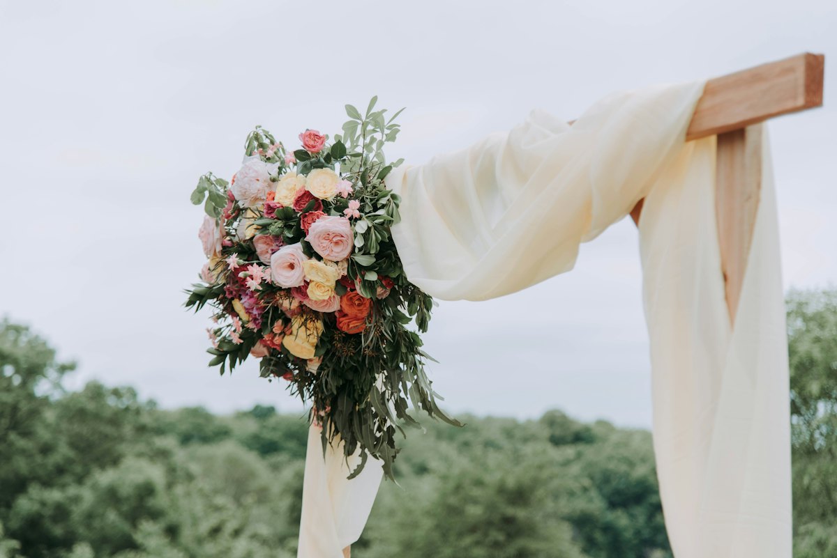 Arcadă de ceremonie decorată cu flori și material textil alb